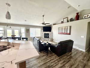 Living room with dark wood-style floors, a textured ceiling, visible vents, ceiling fan, and a fireplace