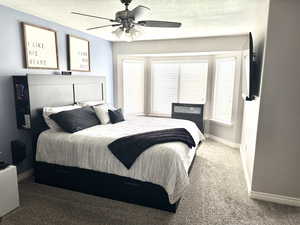 Carpeted bedroom featuring a textured ceiling, a ceiling fan, baseboards, and multiple windows