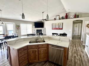 Kitchen with stainless steel dishwasher, a ceiling fan, a stone fireplace, a sink, and open floor plan
