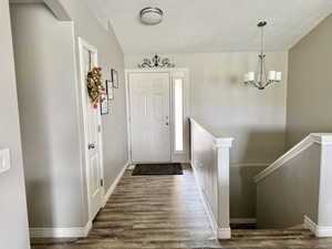 Doorway to outside featuring wood finished floors, baseboards, and an inviting chandelier