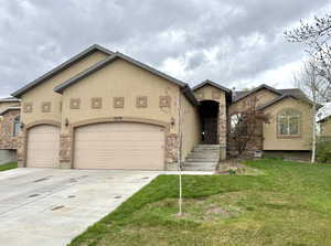 View of front of home with a front lawn, stucco siding, an attached garage, concrete driveway, and stone siding