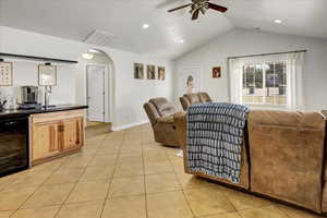Living room featuring vaulted ceiling, light tile patterned floors, ceiling fan, arched walkways, and wine cooler