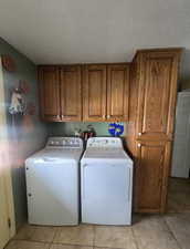 Laundry area with washing machine and clothes dryer, cabinet space, a textured ceiling, and light tile patterned floors