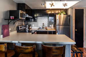 Kitchen with light countertops, appliances with stainless steel finishes, under cabinet range hood, and a sink