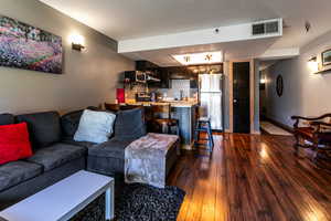 Living area with dark wood-type flooring, visible vents, and baseboards