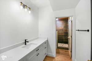 Bathroom with baseboards, wood finished floors, vanity, and tiled shower