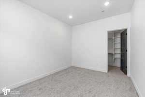 Unfurnished bedroom featuring a closet, a spacious closet, carpet, baseboards, and recessed lighting