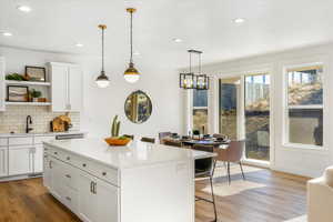 Kitchen featuring a kitchen breakfast bar, open shelves, a sink, light wood-style flooring, and tasteful backsplash