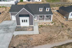View of front facade featuring a porch, a shingled roof, driveway, and fence