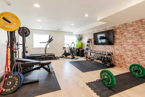 Workout room featuring brick wall, baseboards, wood finished floors, and recessed lighting