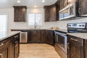 Kitchen with light stone counters, a sink, dark brown cabinetry, light wood-style flooring, and appliances with stainless steel finishes