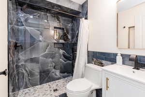 Full bathroom with toilet, tile walls, wainscoting, a tile shower, and vanity