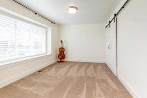 Unfurnished room with visible vents, light carpet, baseboards, and a barn door