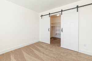 Unfurnished bedroom with a barn door, a closet, a walk in closet, light carpet, and baseboards