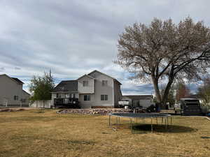 Back of property with a trampoline, a yard, a wooden deck, and fence