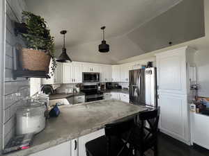 Kitchen with white cabinets, a peninsula, stainless steel appliances, decorative backsplash, and a breakfast bar area