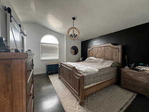 Bedroom featuring dark wood finished floors, an inviting chandelier, a barn door, and lofted ceiling