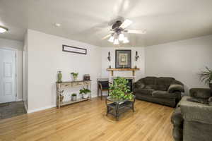 Living area featuring light wood-type flooring, baseboards, a fireplace, and ceiling fan
