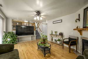 Living area with light wood-type flooring, baseboards, a ceiling fan, a brick fireplace, and stairway