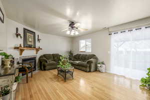 Living room with visible vents, light wood-type flooring, baseboards, a glass covered fireplace, and ceiling fan