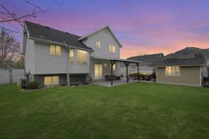 Back of property at dusk with a patio area, fence, and a yard