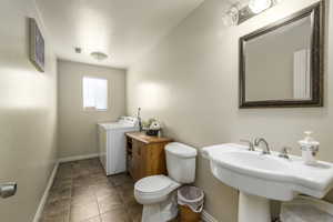 Bathroom with visible vents, toilet, a sink, baseboards, and washer / clothes dryer
