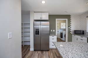 Kitchen featuring washer / clothes dryer, white cabinetry, light stone countertops, appliances with stainless steel finishes, and wood finished floors