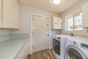 Laundry area with light wood-style floors, washing machine and clothes dryer, and cabinet space