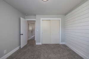 Unfurnished bedroom with a textured ceiling, a closet, carpet flooring, and wooden walls