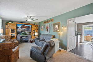Living room with a fireplace, a ceiling fan, a textured ceiling, and carpet
