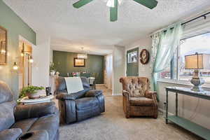 Living room with ceiling fan with notable chandelier, baseboards, carpet flooring, and a textured ceiling