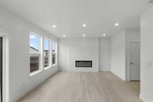 Living room featuring recessed lighting, light wood-type flooring, a fireplace, and large windows