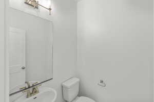 Half bathroom with toilet and a sink located off garage and mudroom