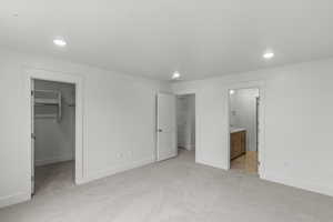 Primary bedroom featuring ensuite bathroom, a walk in closet, light carpet, and recessed lighting