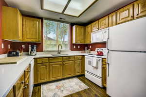 Kitchen featuring dark wood finished floors, white appliances, visible vents, light countertops, and a sink