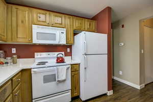 Kitchen featuring dark wood-style flooring, light countertops, baseboards, and white appliances