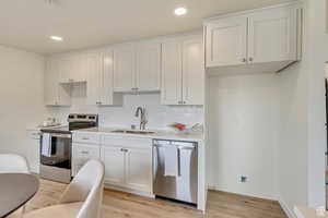 Kitchen with appliances with stainless steel finishes, a sink, white cabinetry, and light wood-style floors