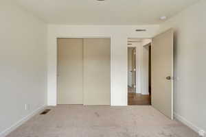 Unfurnished bedroom with carpet floors, visible vents, and a closet