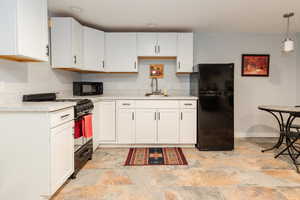 Kitchen with a sink, stone finish flooring, black appliances, light countertops, and white cabinets
