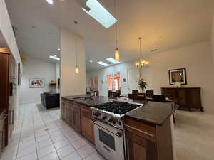 Kitchen with vaulted ceiling with skylight, dark stone countertops, a sink, high end range, and pendant lighting