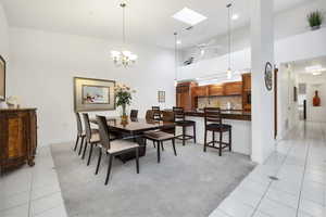 Dining space featuring light colored carpet, light tile patterned floors, a towering ceiling, and a skylight