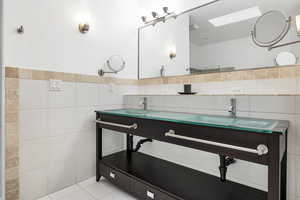 Full bathroom featuring tile patterned floors, a wainscoted wall, a sink, tile walls, and a skylight