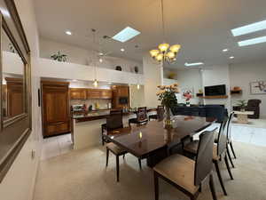 Dining area with a skylight, light tile patterned flooring, and ceiling fan with notable chandelier