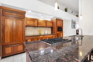 Kitchen with a sink, brown cabinets, built in appliances, decorative light fixtures, and backsplash
