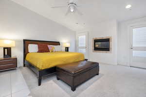 Carpeted bedroom featuring tile patterned floors, a tiled fireplace, baseboards, lofted ceiling, and ceiling fan