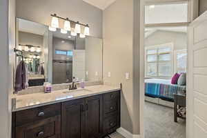 Bathroom with ensuite bathroom, baseboards, a shower stall, vanity, and vaulted ceiling