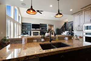 Kitchen with decorative light fixtures, a sink, a stone fireplace, white microwave, and light stone countertops