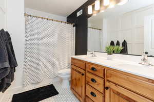 Full bath with double vanity, visible vents, toilet, and a sink