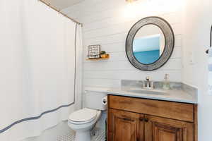 Bathroom featuring tile patterned flooring, wood walls, toilet, vanity, and a shower with shower curtain