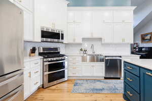Kitchen with blue cabinetry, white cabinetry, stainless steel appliances, and a sink